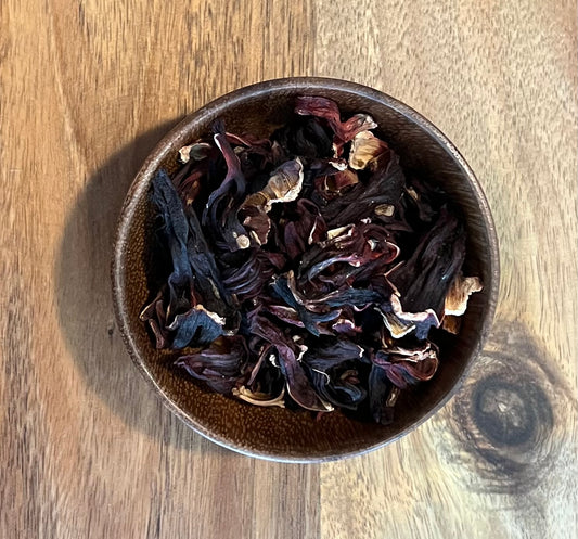 Dried hibiscus flowers in a small brown ceramic bowl, placed on a wooden tabletop.