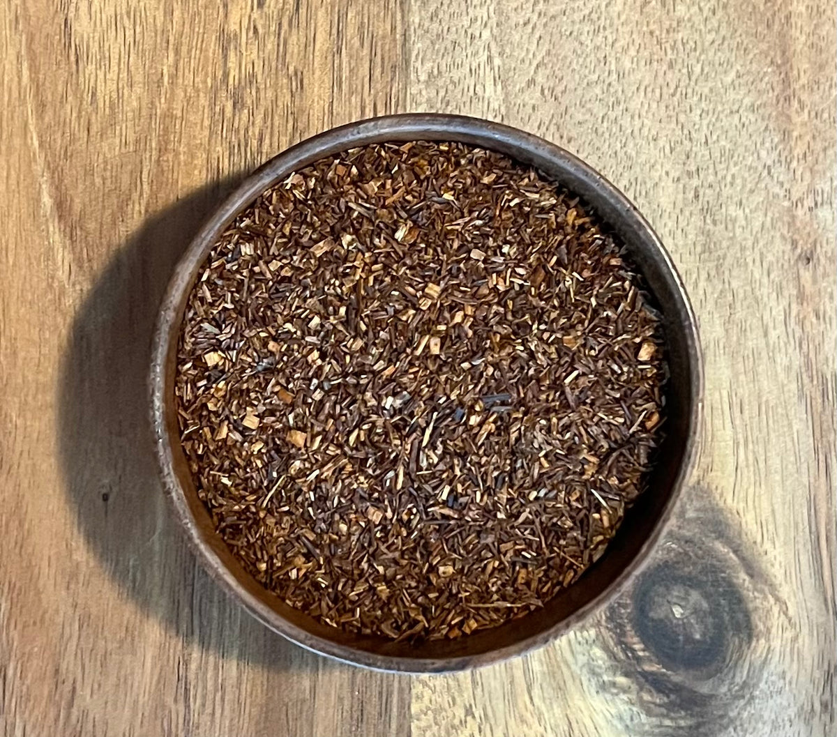 A top-down view of loose-leaf Red Rooibos leaves wooden acacia bowl, set on a wooden tabletop.