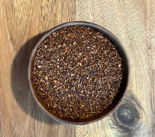 A top-down view of loose-leaf Red Rooibos leaves wooden acacia bowl, set on a wooden tabletop.